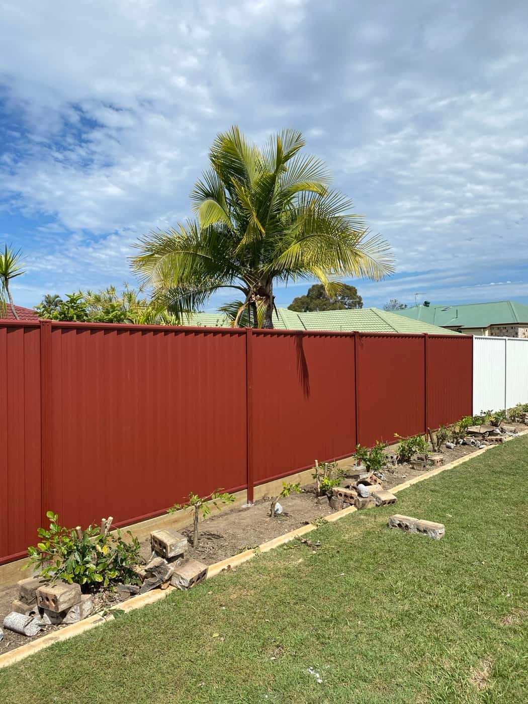 Long red Colorbond boundary fence along a garden bed