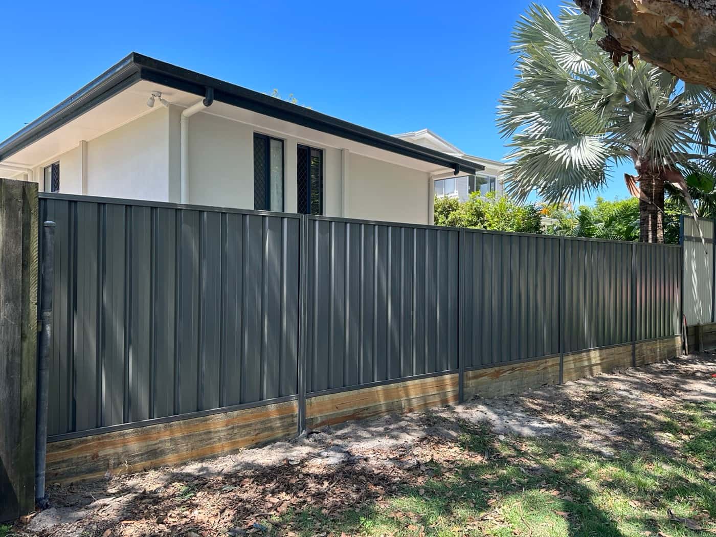 Dark Colorbond fence on timber sleepers beside a house