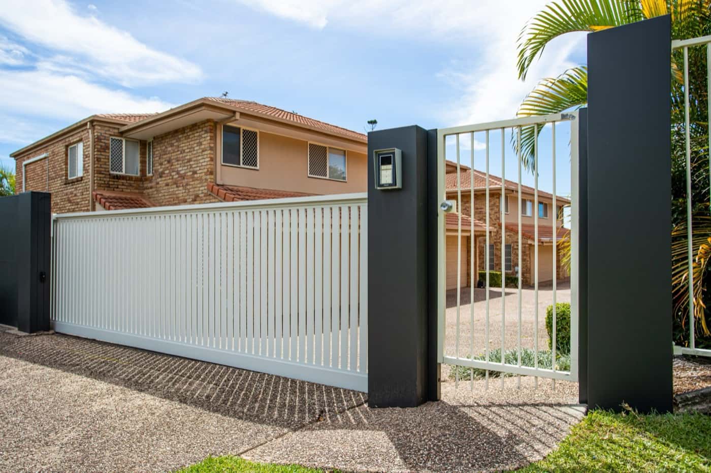 White slat sliding driveway gate between dark rendered pillars