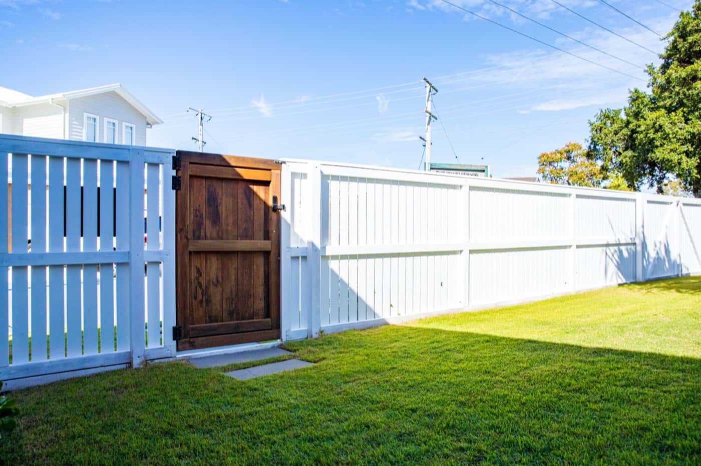 Stained timber gate set in a white slat fence